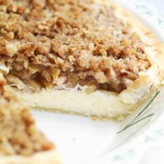 Apple pie cheesecake with one slice removed to show creamy cheesecake layer and streusel topping.