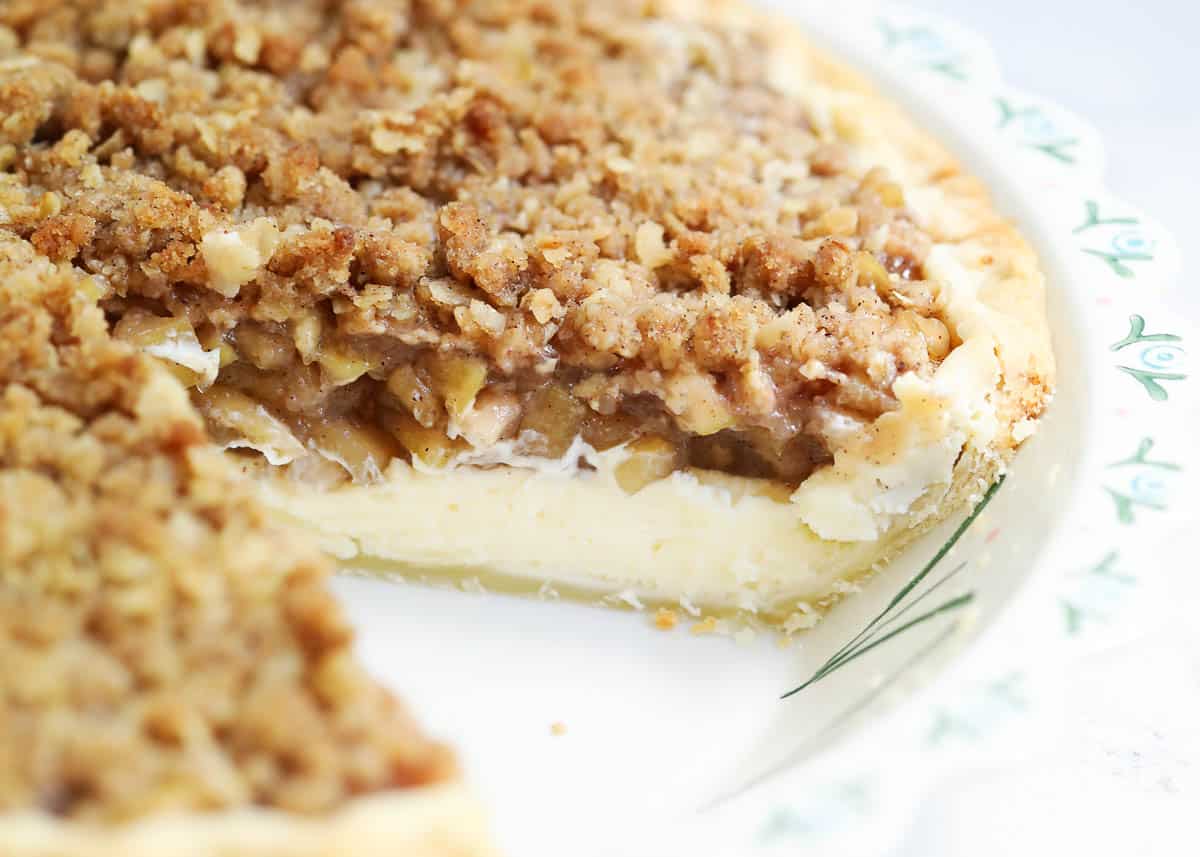 Apple pie cheesecake in a pie pan with a slice taken out of it. 