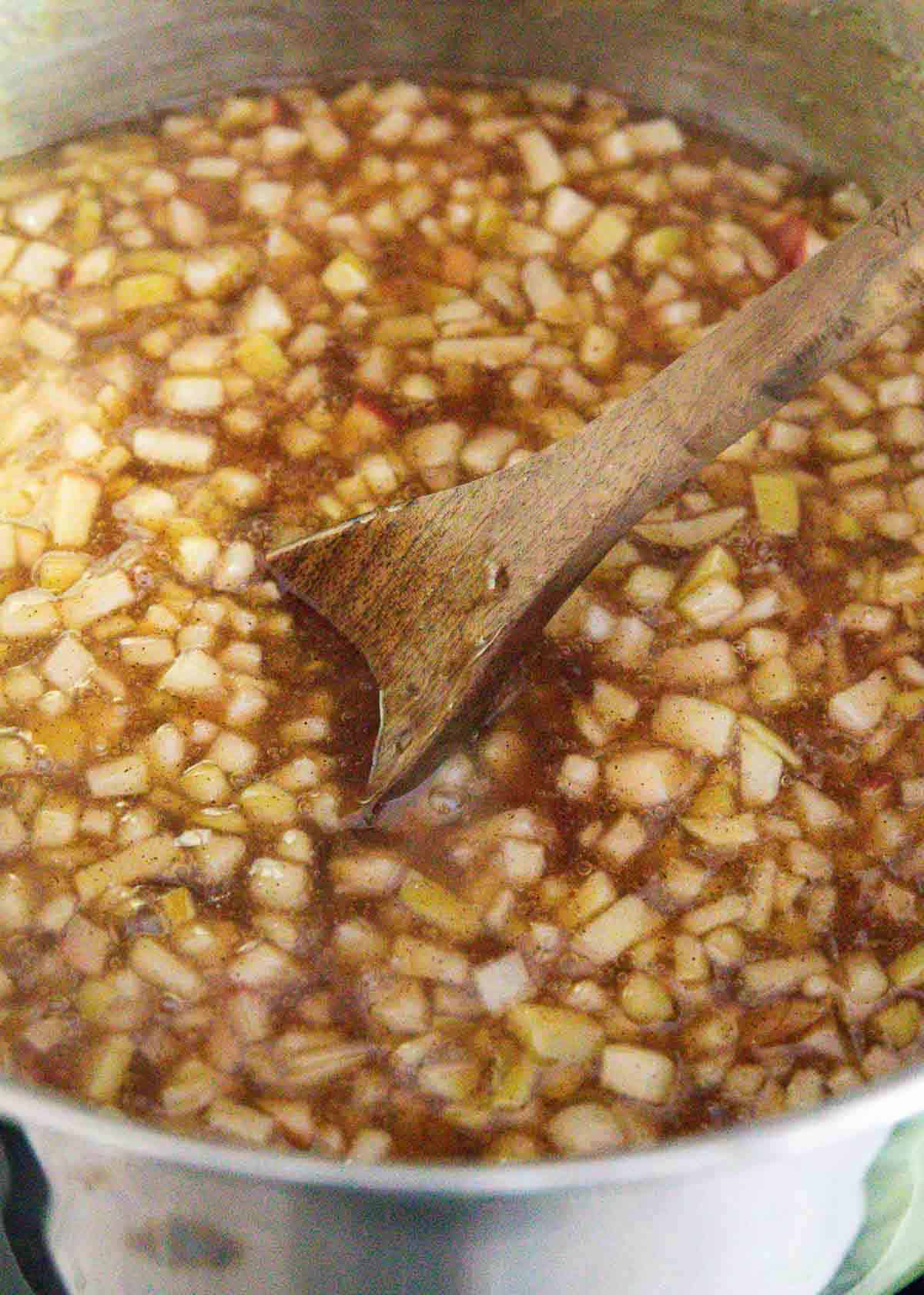 Apple pie filling in a pot stirred with a wooden spoon. 