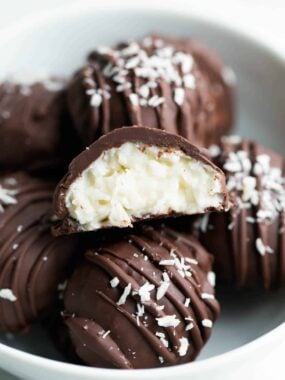 Chocolate coconut balls in a bowl with a bite removed to show chewy texture and chocolate coating.