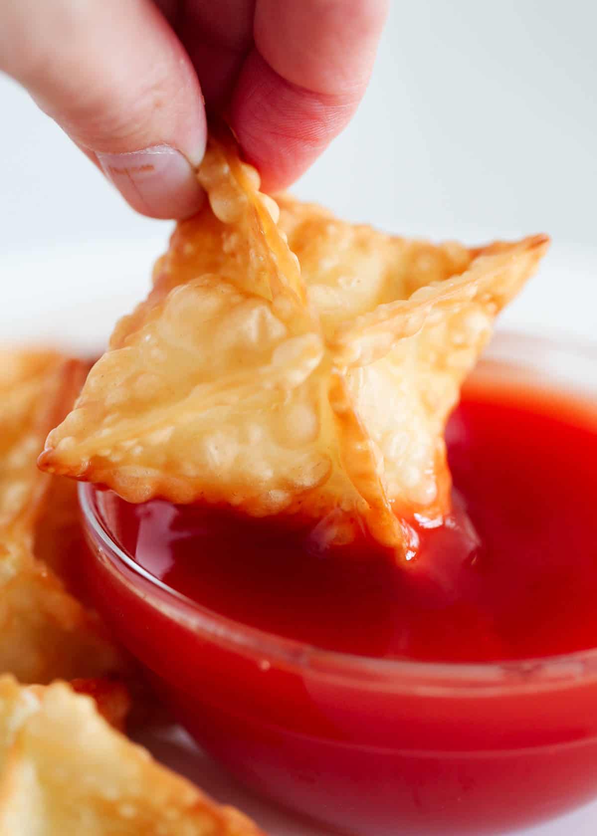 Dipping cream cheese wontons in sweet and sour sauce. 