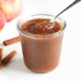 Apple butter in a glass jar with spoon.