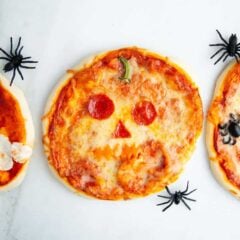 Halloween pizzas decorated like a jack-o-lantern, spider and ghosts on the counter.