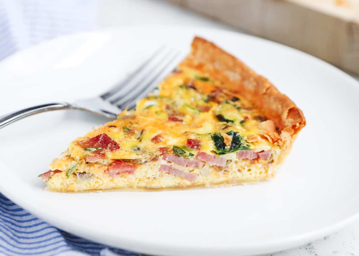 Slice of ham and cheese quiche on a white plate.