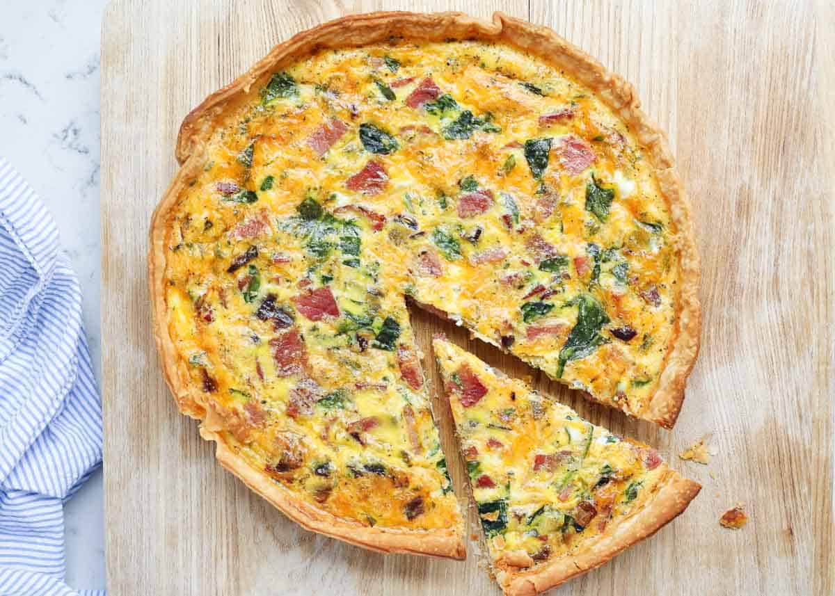 Sliced ham and quiche recipe on a board.