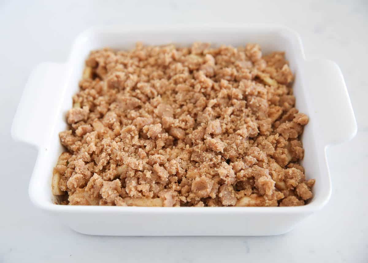 Unbaked apple crumble in a white square baking dish with a generous layer of brown sugar crumble topping.