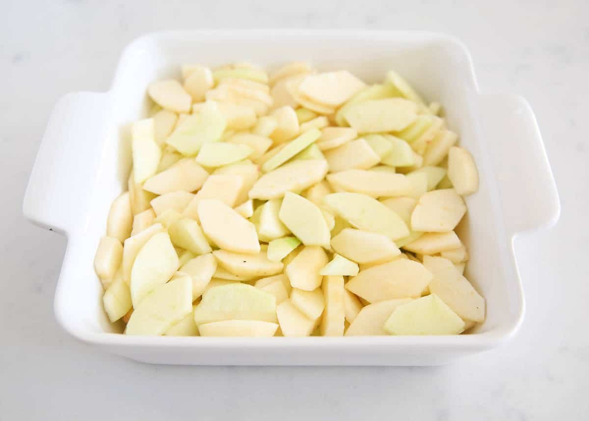 Thinly sliced peeled apples arranged evenly in a white square baking dish.