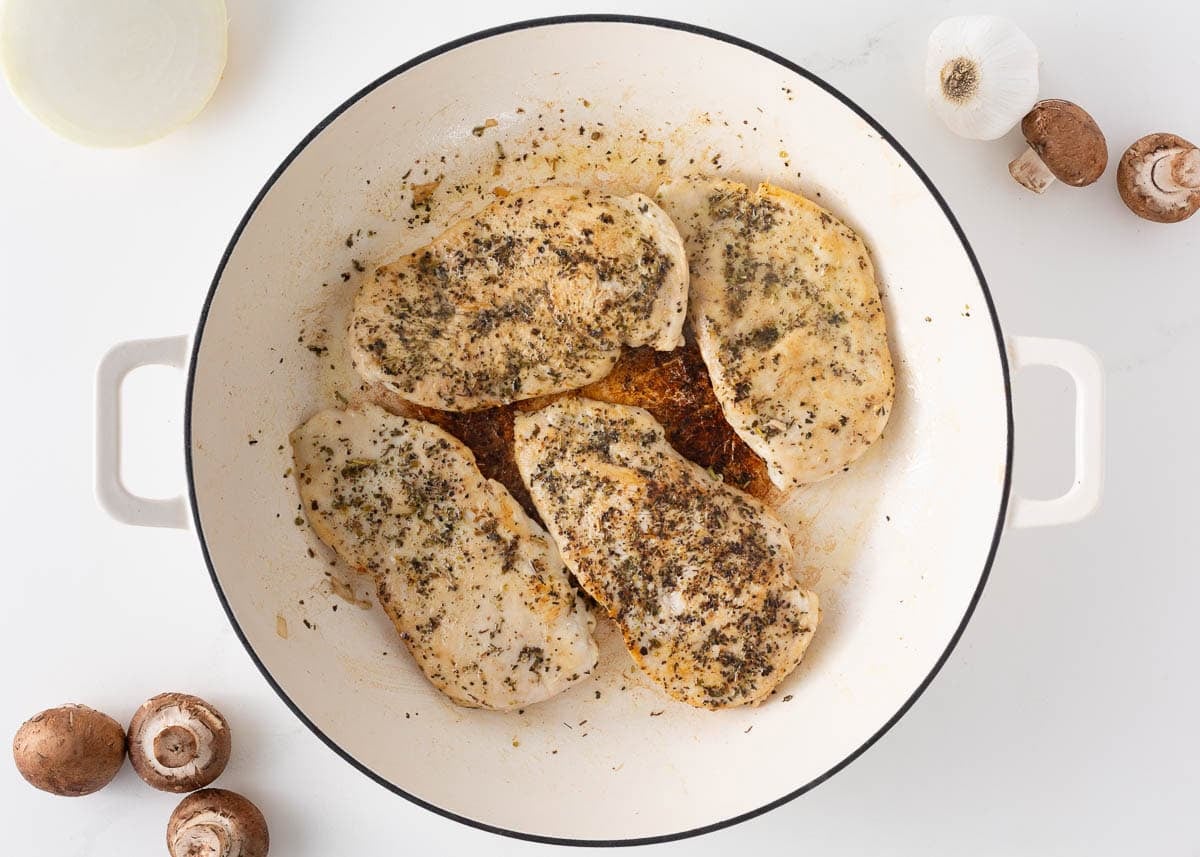 Seasoned chicken breasts searing in a skillet until golden brown.