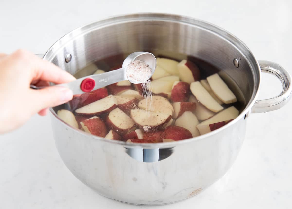 Pouring salt into pot of red potatoes.