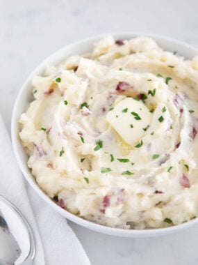 Garlic mashed red potatoes in a white serving bowl garnished with butter.