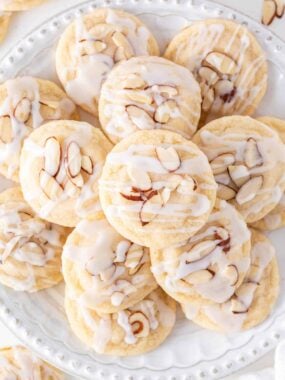 Almond cookies topped with a simple glaze on a white plate.