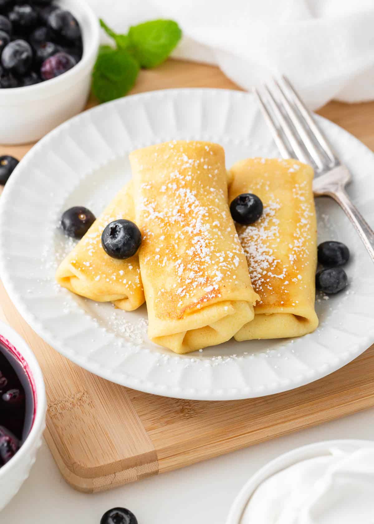 Looking for a unique breakfast experience? Try your hand at making cheese blintzes! Learn how to make these stuffed delights for your next cozy breakfast or brunch at home. Blintzes on a white plate.
