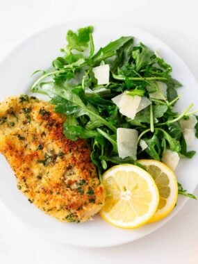 Chicken milanese with arugula salad on a plate with lemon slices.