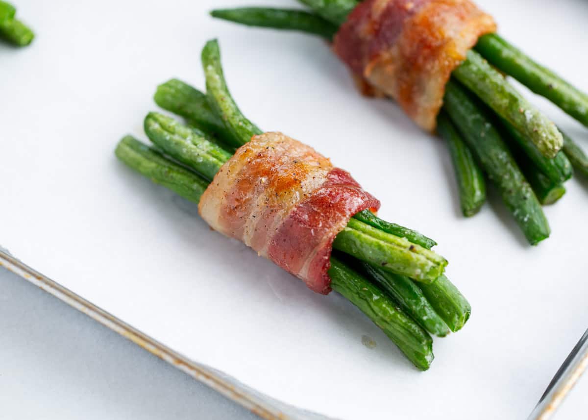 Impressive and elegant yet so easy to make these crispy bacon wrapped green bean bundles are the best savory side dish to enjoy this holiday season! Green bean bundles on baking sheet.