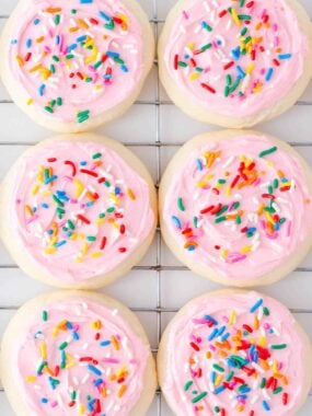Soft, bakery style Lofthouse cookies recipe topped with fluffy pink frosting on a cooling rack.