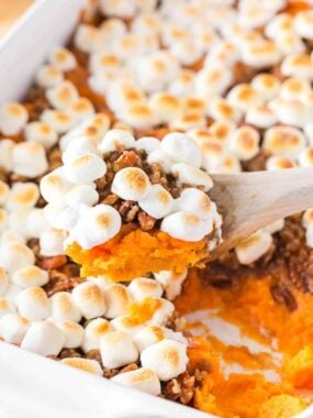 Sweet potato casserole with marshmallows being served out of a baking dish showing creamy sweet potatoes, crunchy pecans and gooey marshmallows.