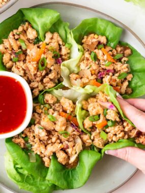 Close-up of someone holding a Thai chicken lettuce wrap, ready to eat.