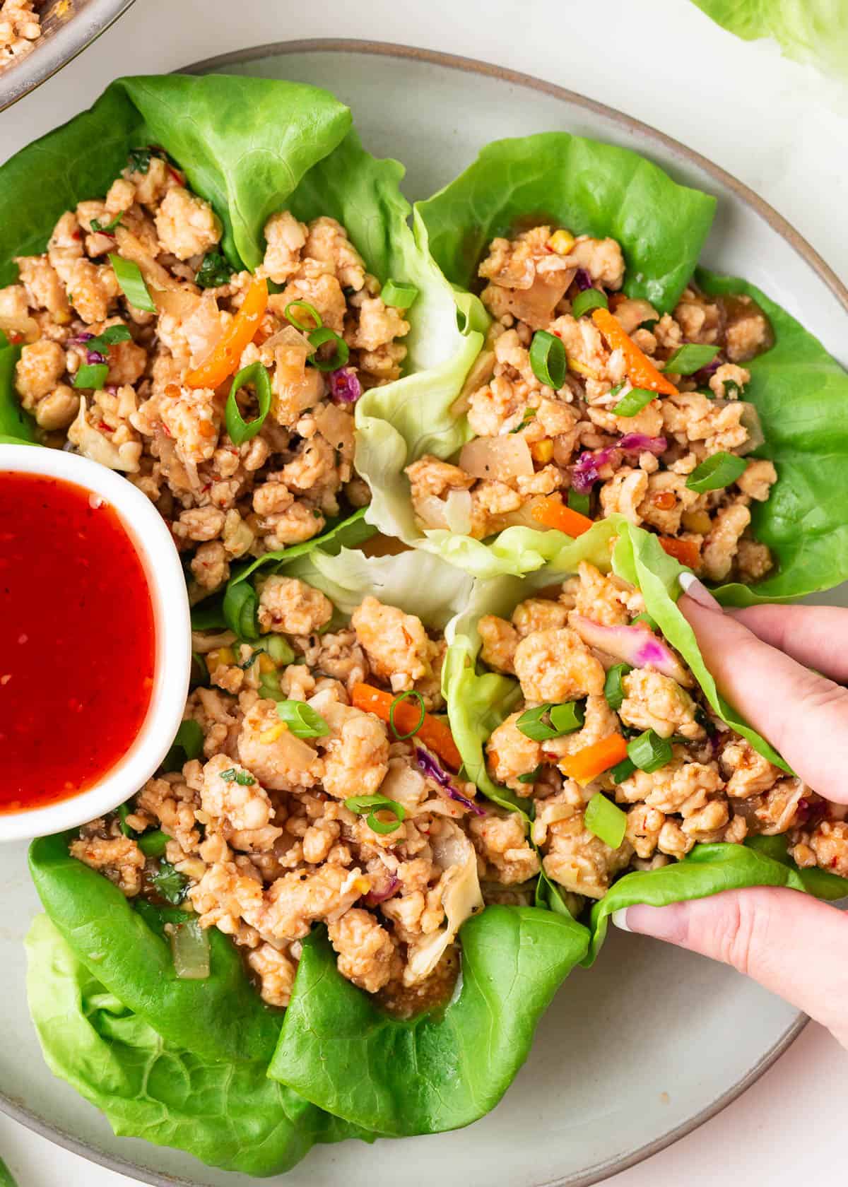 Send your taste buds into overdrive with these fresh, healthy, and utterly delicious Thai chicken lettuce wraps. Made in under 30 minutes, the sweet, savory, and spicy filling will have you licking your fingers! Thai chicken lettuce wraps with sauce on the side.