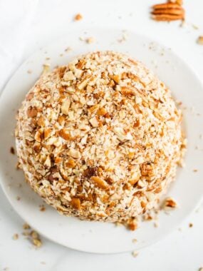 Top view of a cheese ball coated in chopped pecans on a white plate, part of an easy cheese ball recipe perfect for entertaining.