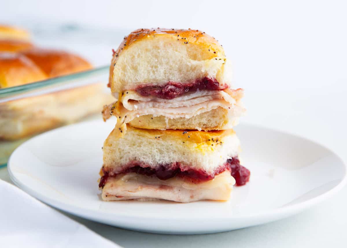 Sweet and savory with a buttery drizzle, these turkey cranberry sliders are the best way to use Thanksgiving leftovers. Turkey slices and cranberry sauce are sandwiched between Hawaiian rolls then baked to golden brown for the ultimate meal or snack! Easy turkey cranberry sliders on a plate.