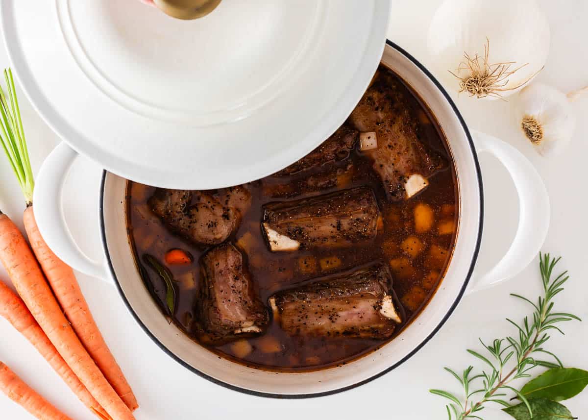 Beef short ribs in a pot with the lid half on with veggies.