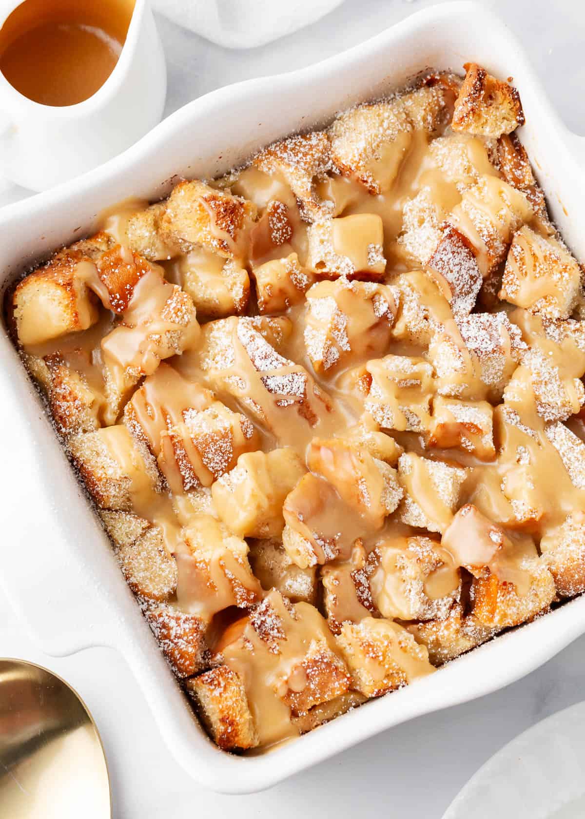 Bread pudding with caramel sauce in a white baking dish.