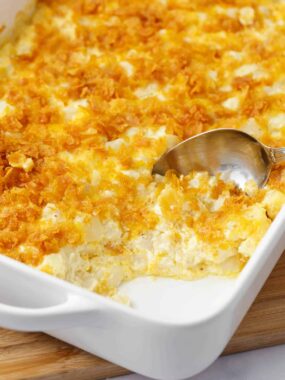 Spoonful of cheesy potatoes in a white casserole dish.