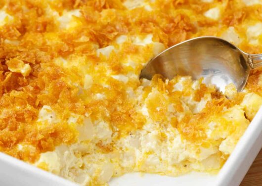 Spoonful of cheesy potatoes in a white baking dish.