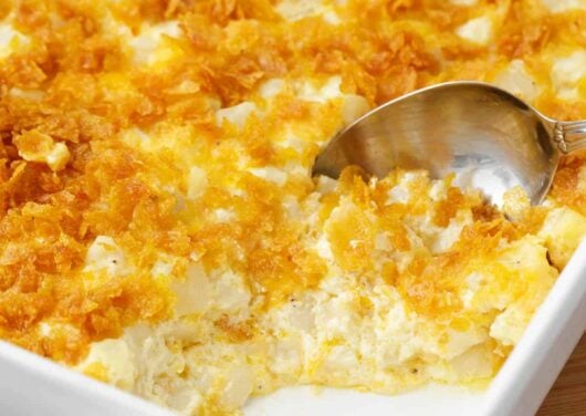 Spoonful of cheesy potatoes in a white casserole dish.