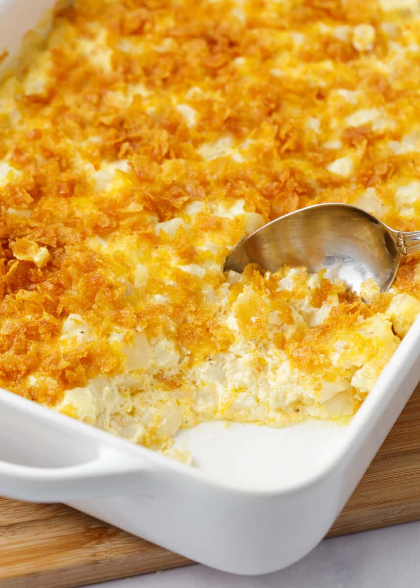Spoonful of cheesy potatoes in a white casserole dish.