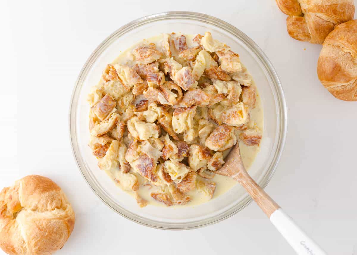 Combining croissant cubes and creamy egg mixture in a bowl.