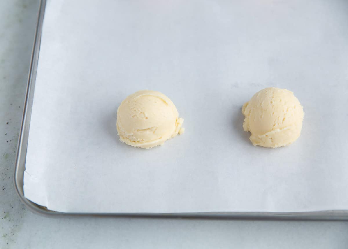Cream cheese cookie dough balls on parchment lined cookie sheet.