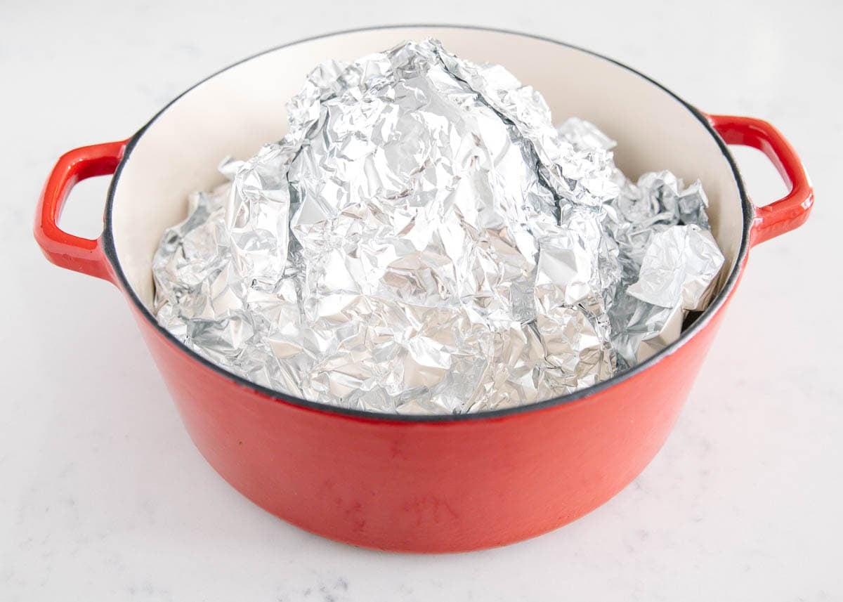 Foil-covered baked ham in a red Dutch oven, ready to bake in the oven.