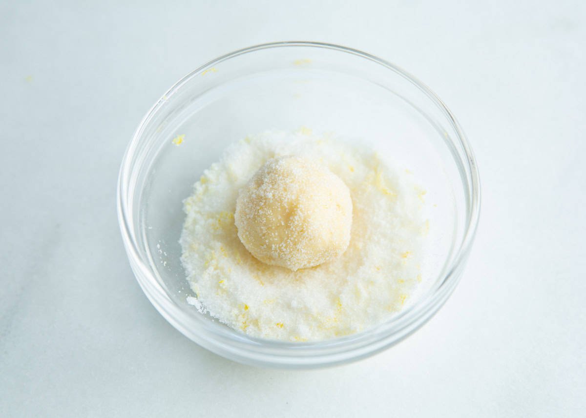 Rolling cookie dough ball into granulated sugar with lemon zest.