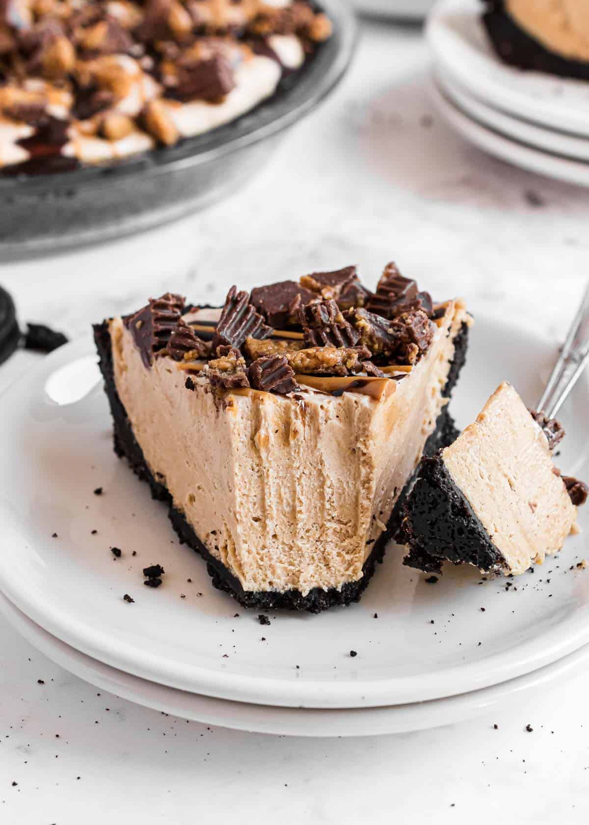 Slice of oreo peanut butter pie on a plate with chopped peanut butter cups on top.