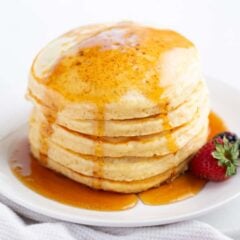 Stack of fluffy homemade pancakes topped with butter and maple syrup on a white plate.