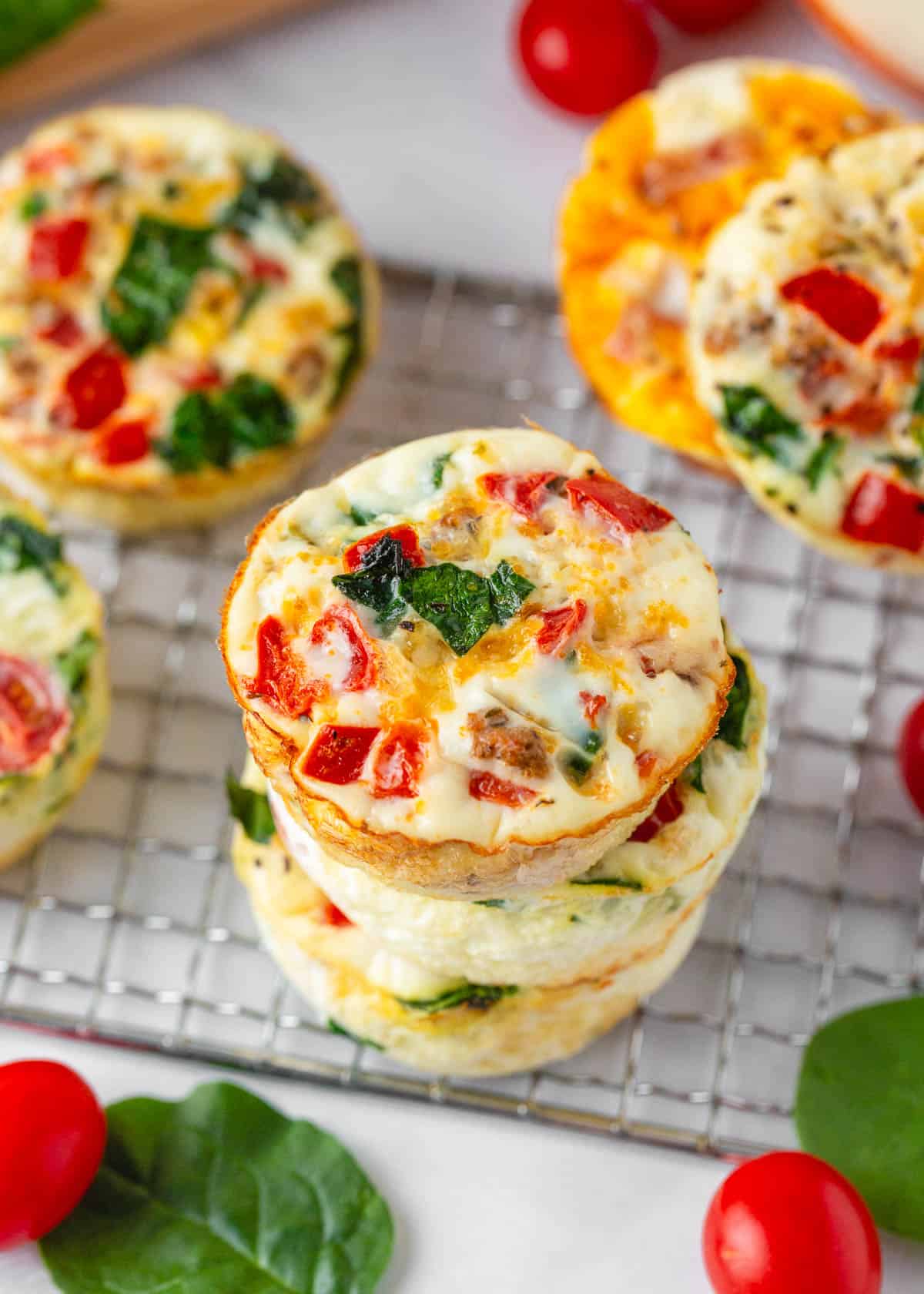 Easy-to-customize egg white muffins that make the perfect healthy on-the-go breakfast. They're high in protein, low in fat and downright delicious! Colorful egg white muffins stacked on a cooling rack, packed with spinach, tomatoes, and cheese.