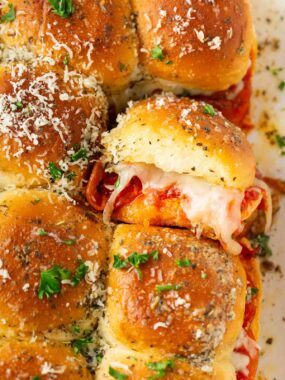 Pepperoni pizza sliders made with Hawaiian rolls on a baking sheet.