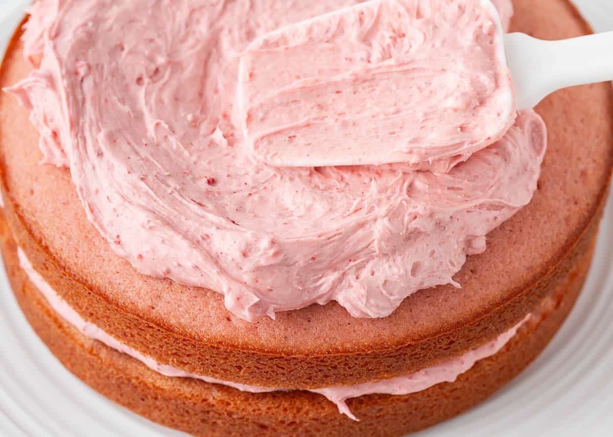 Spreading strawberry frosting onto a strawberry cake.