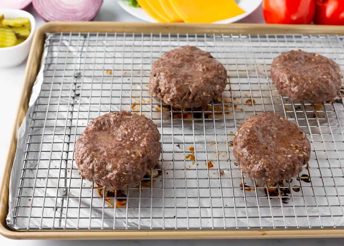Juicy baked hamburgers cooked in the oven on a wire rack over a baking sheet.