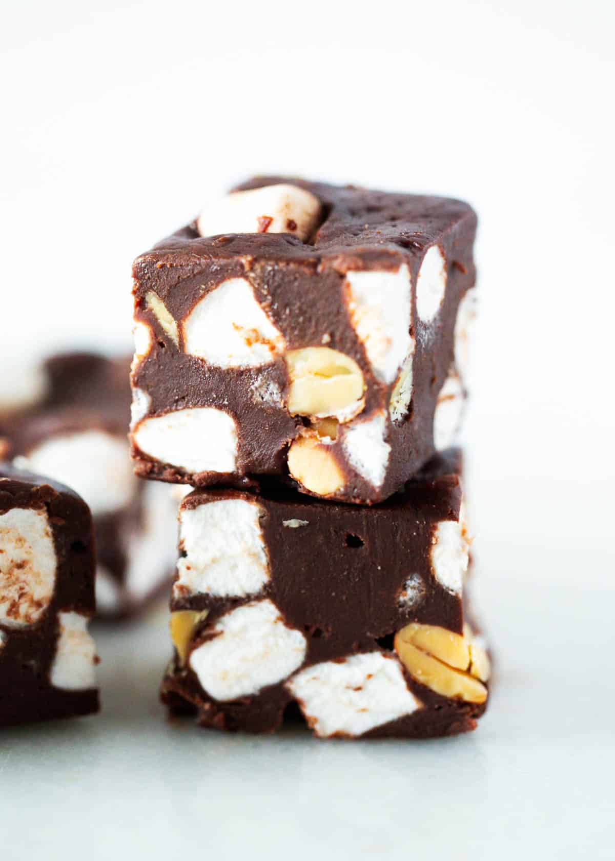 Rich and decadent rocky road fudge is an easy chocolate fudge recipe loaded with mini marshmallows and peanuts. Every bite is an indulgent sweet, salty, crunchy and chewy taste. The best rocky road fudge stacked on a plate.