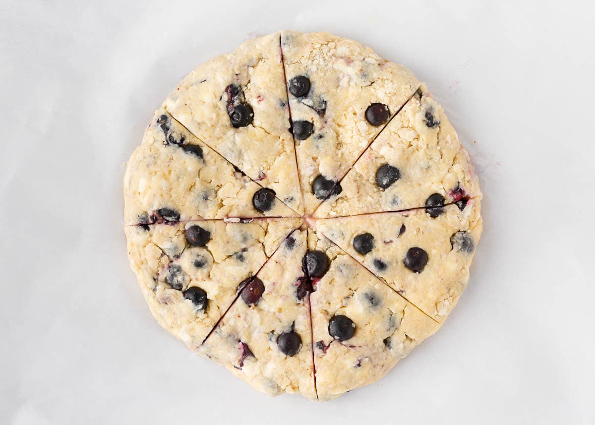 Blueberry scone dough in a circle shape and cut into wedges.