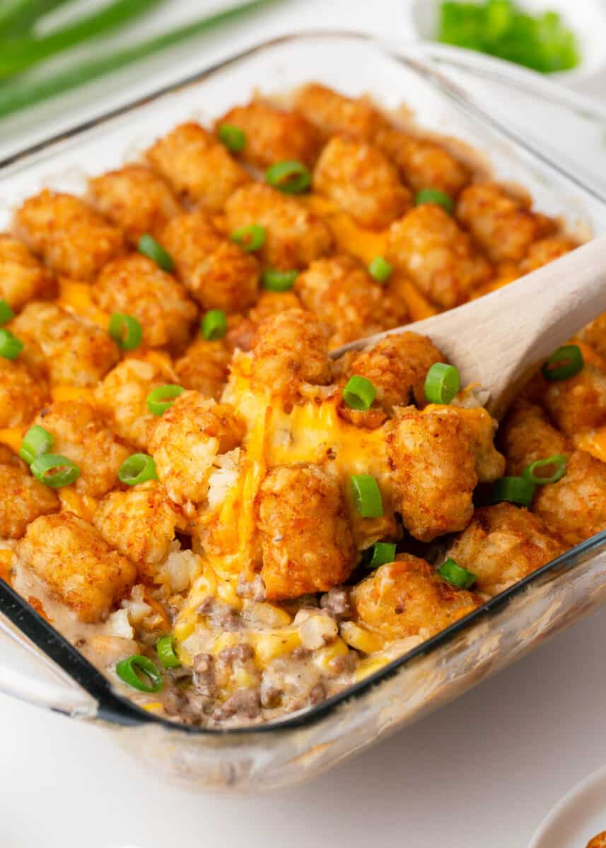 Tater tot casserole in a glass dish with a spoon.