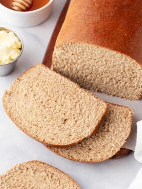 Top down photo of whole wheat bread with a few slices and both butter and honey to the side for serving.