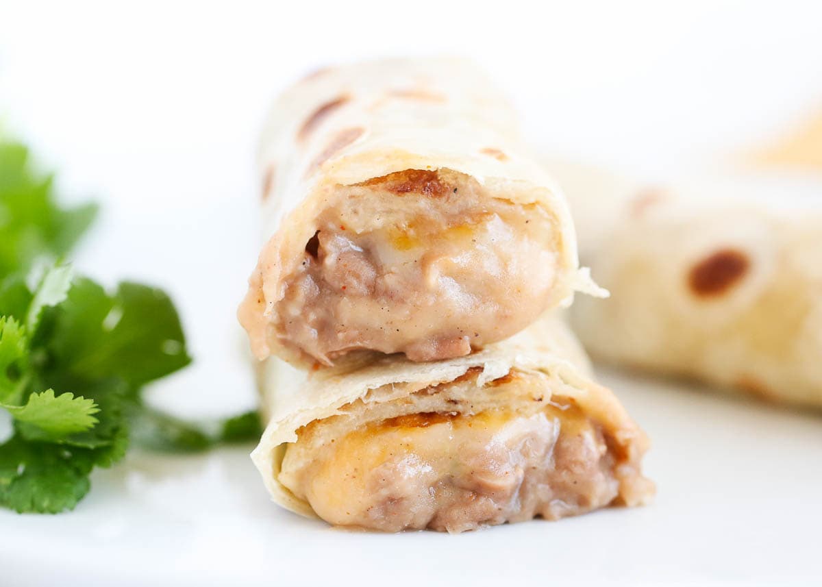 Bean and cheese burritos with cilantro on a white plate.