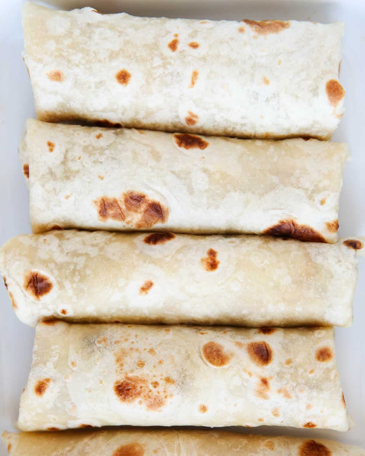 Bean burritos laying in a white baking dish.