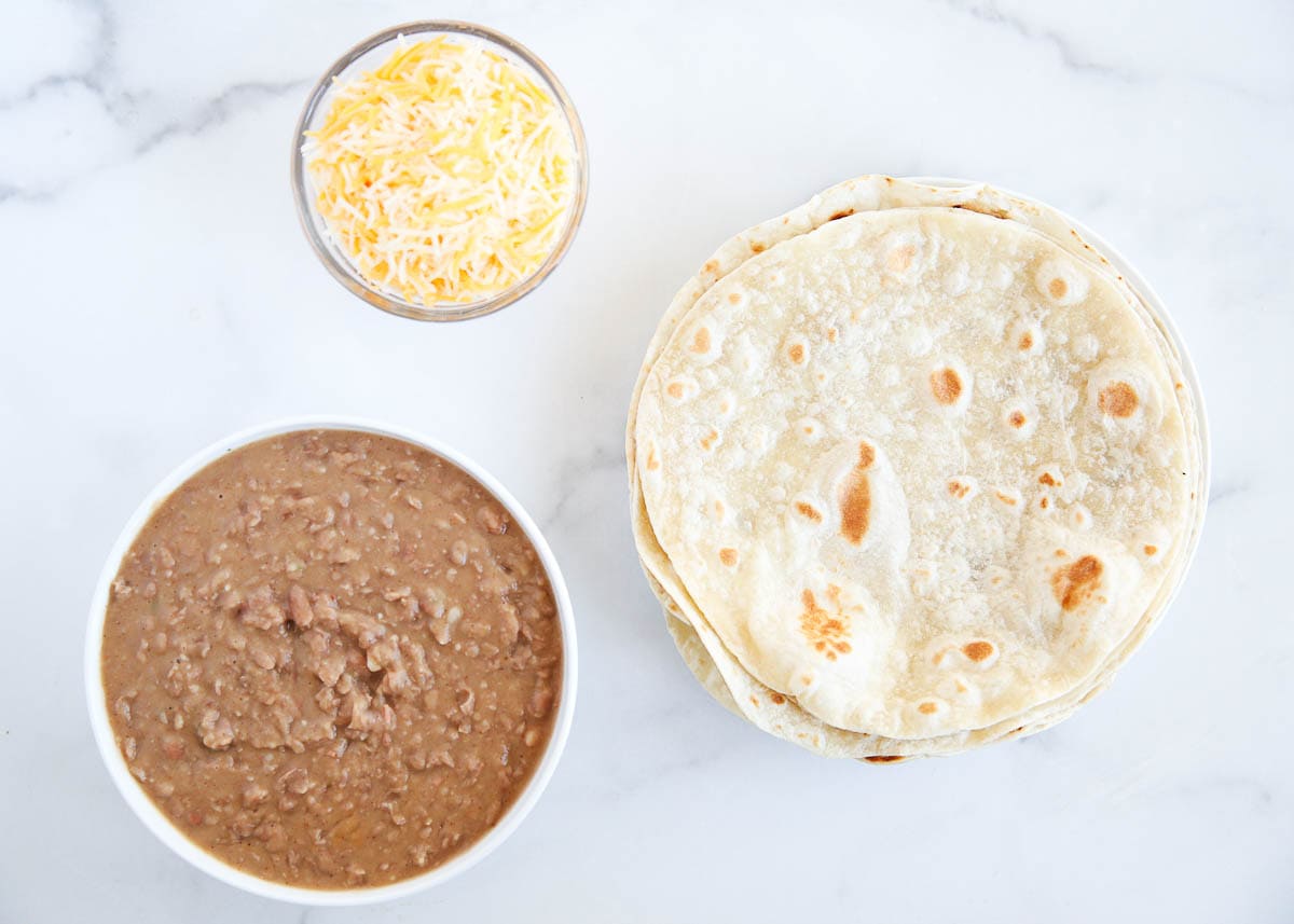 Beans, tortillas and cheese sitting on a countertop.