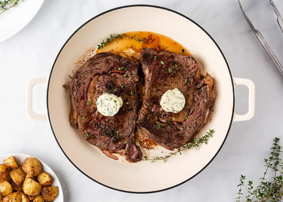 Seared steak in cast-iron skillet topped with garlic butter and herbs after cooking in the oven.