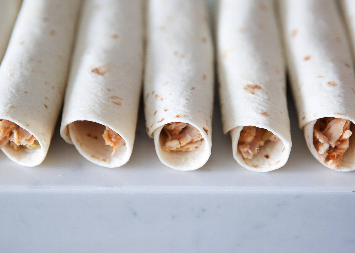 Rolled chicken flautas lined up on a counter before frying.