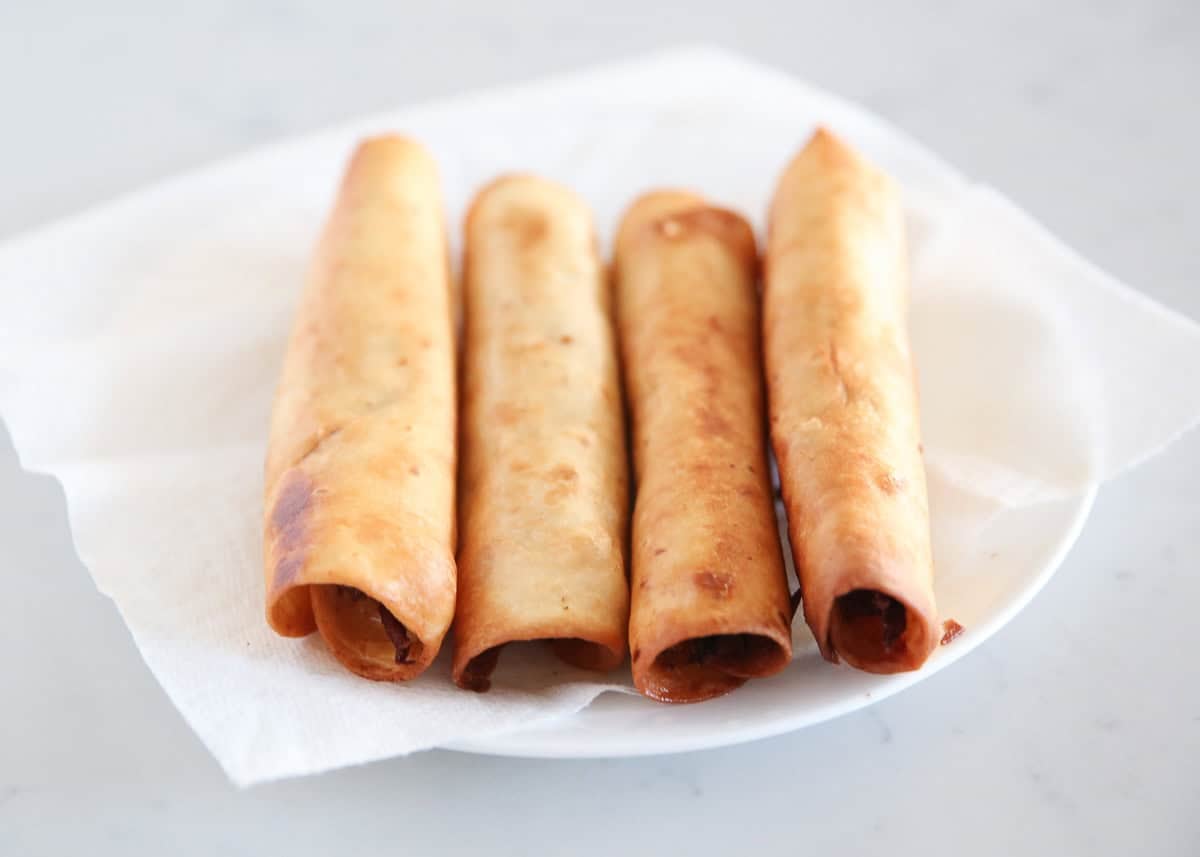 Crispy fried chicken flautas draining on a paper towel-lined plate.